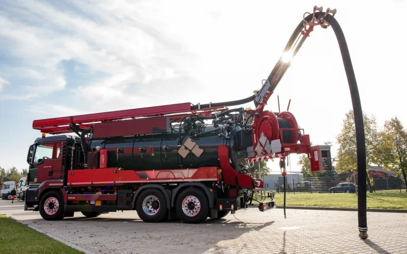 Red and black KROLL combination vehicle with extended telescopic boom, suction hose reaching down to the ground