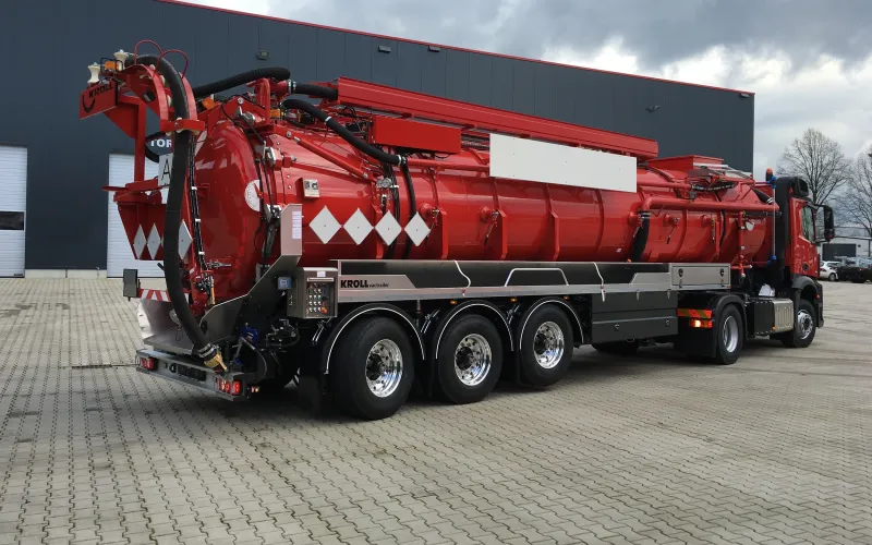 Red three-axle vacuum semi-trailer with suction hose at the rear, oblique view in front of the KROLL hall