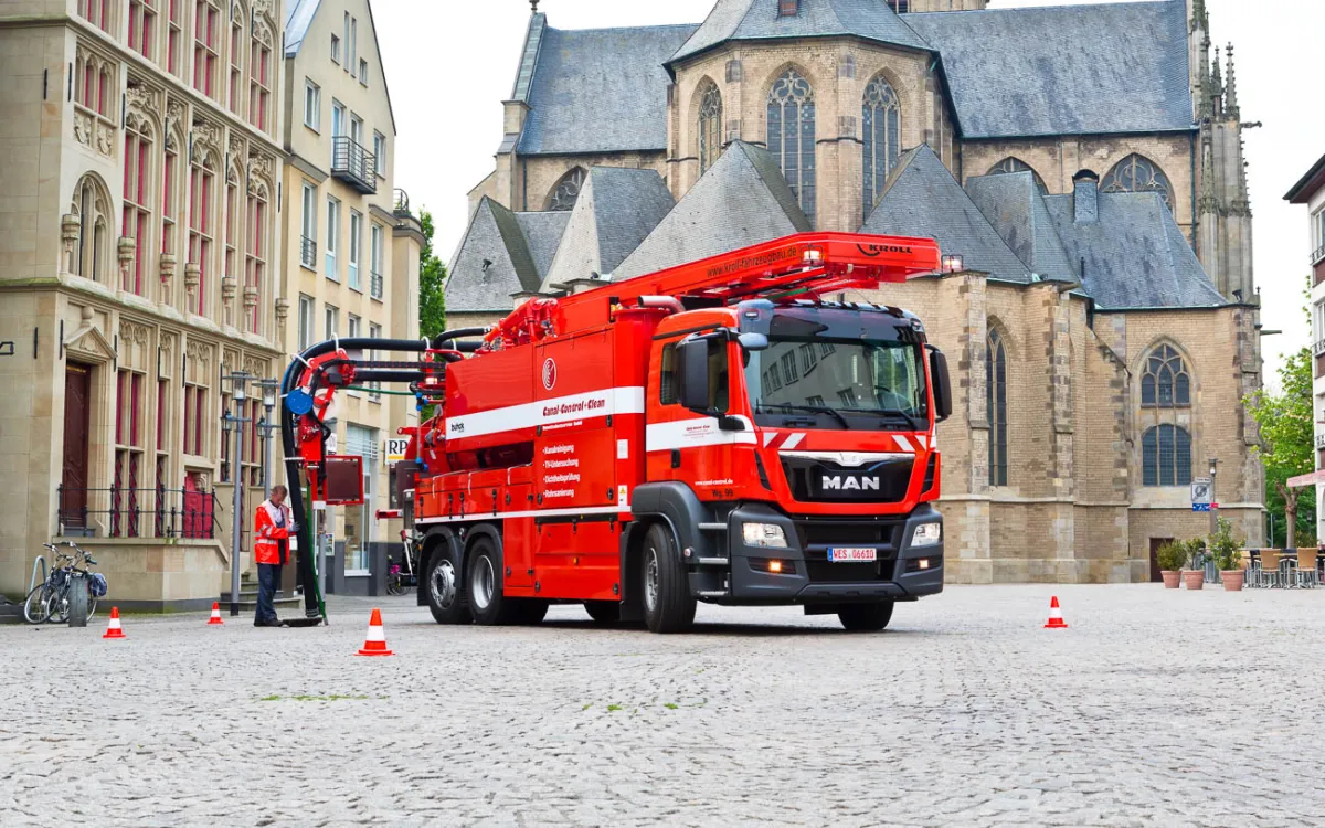 Red KROLL WRS 2 on a MAN chassis at work on an old town square in front of a church, a worker at the manhole