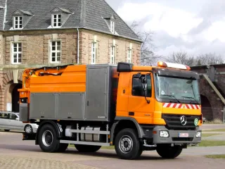 Orange high-pressure jetting vehicle on a Mercedes chassis with stainless steel equipment cabinets in front of a historic brick building
