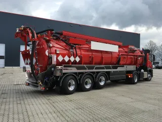 Red three-axle vacuum semi-trailer with suction hose at the rear, oblique view in front of the KROLL hall
