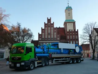 Ciągnik z naczepą ssącą z niebieską zabudową trzykomorową przed zabytkowym ratuszem