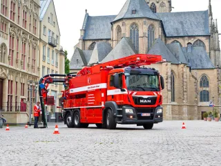 Red KROLL WRS 2 on a MAN chassis at work on an old town square in front of a church, a worker at the manhole